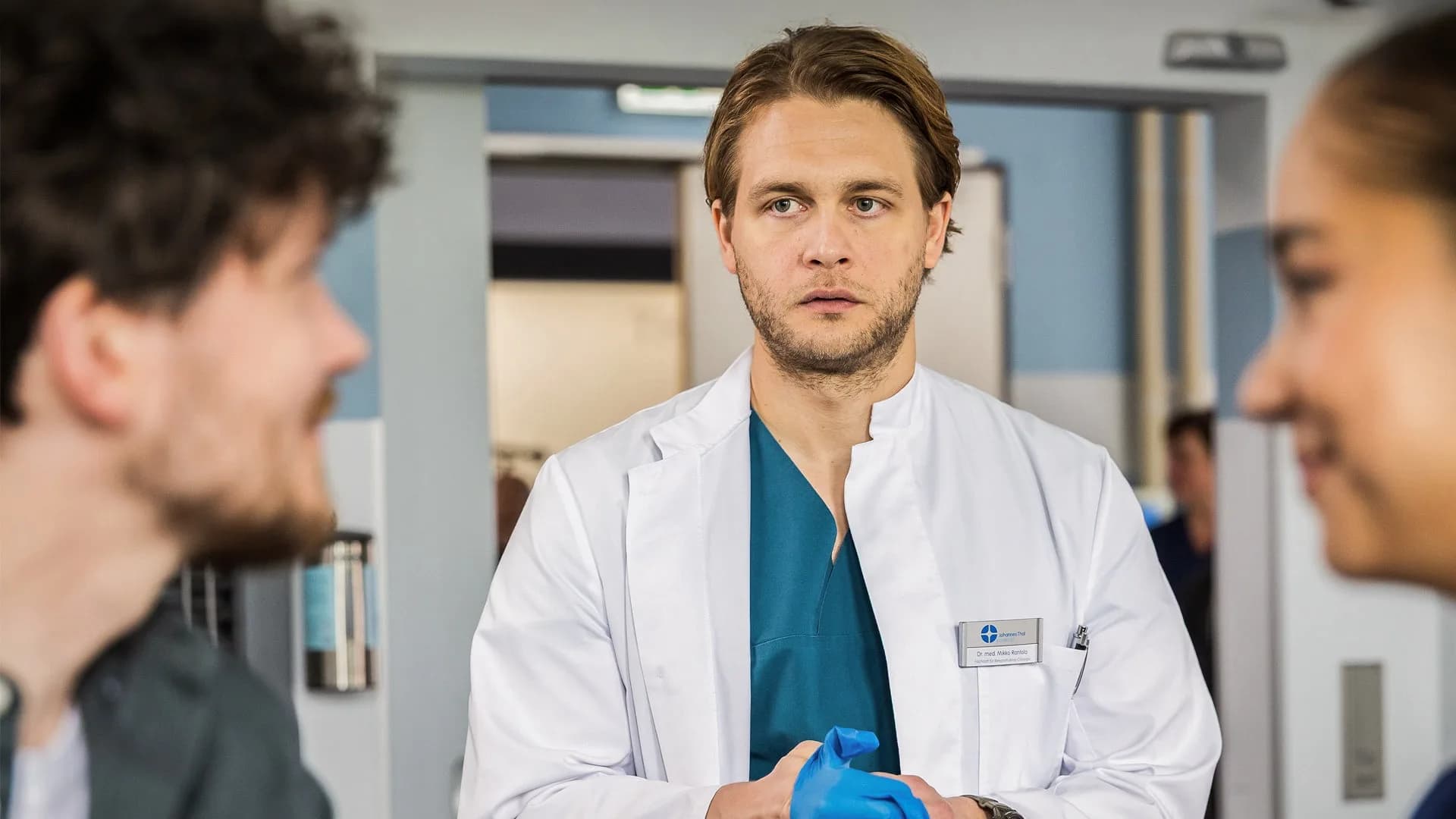 Junge Ärzte Miteinander: Arzt im Gespräch mit zwei Personen in der Klinik — Szenenbild aus In aller Freundschaft – Die